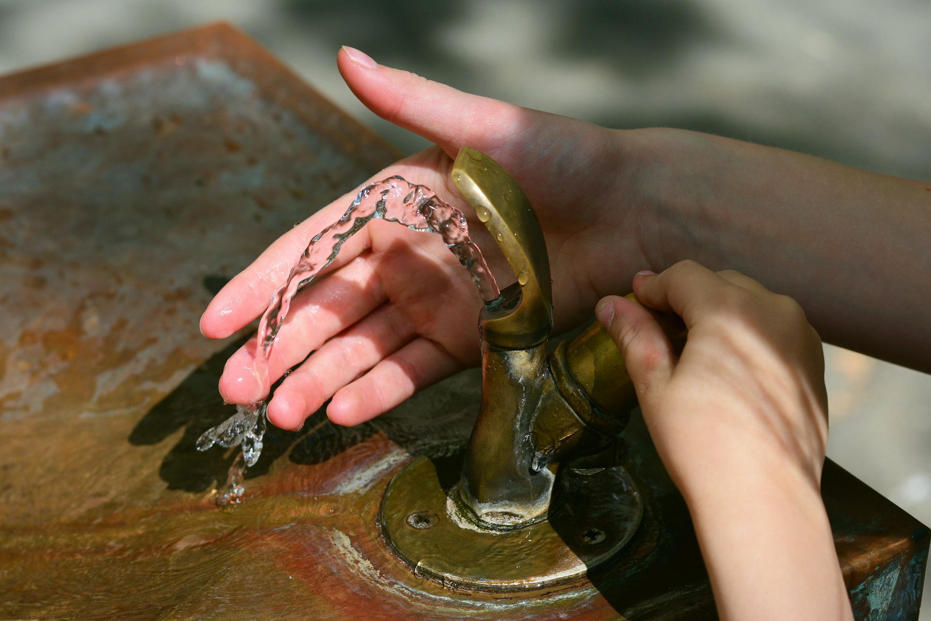 Hände am Wasserhahn des Brunnens